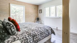Een slaapkamer met een bed, twee ramen, een stoel en een houten vloer.