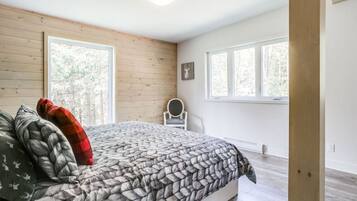 Un dormitorio con una cama, dos ventanas, una silla y suelo de madera.