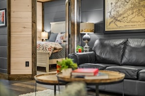 A modern living room with a leather sofa, a round coffee table, and a bed with floral bedding. - Smoky Dream Lodge: Heated Pool, Hot Tub & Games! (Pigeon Forge)
