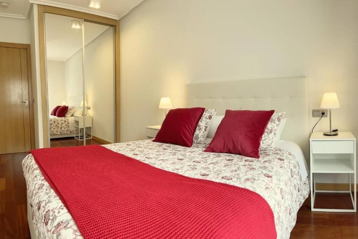 Une chambre à coucher avec un lit, deux tables de chevet, un miroir, une armoire et une couverture rouge.