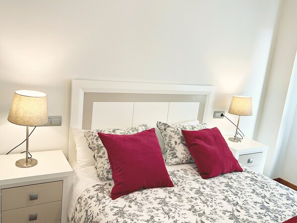 A neatly made bed with floral bedding, two red pillows, and two bedside lamps on white nightstands.