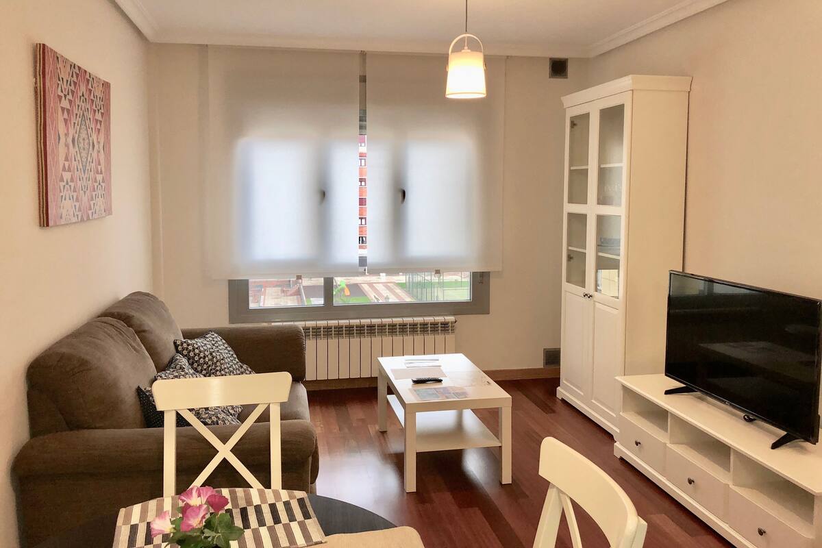 Un salon avec un canapé, une table basse, un téléviseur posé sur un meuble et une fenêtre équipée de stores.