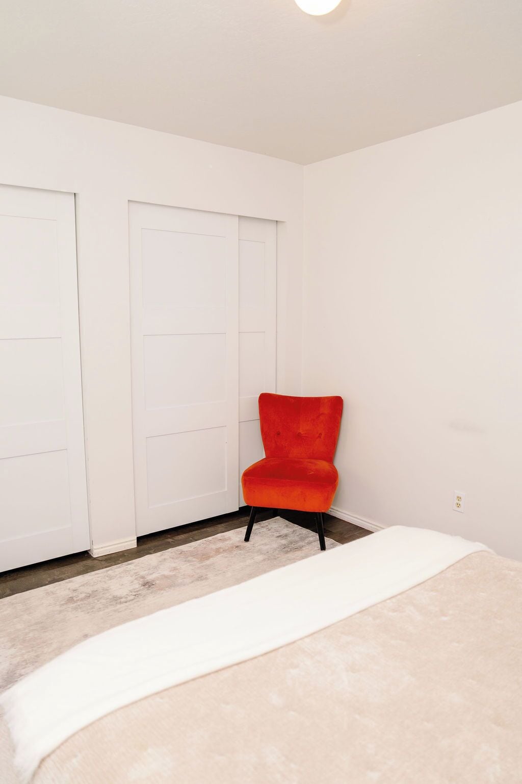 Un dormitorio con una cama, una silla roja y dos puertas blancas.