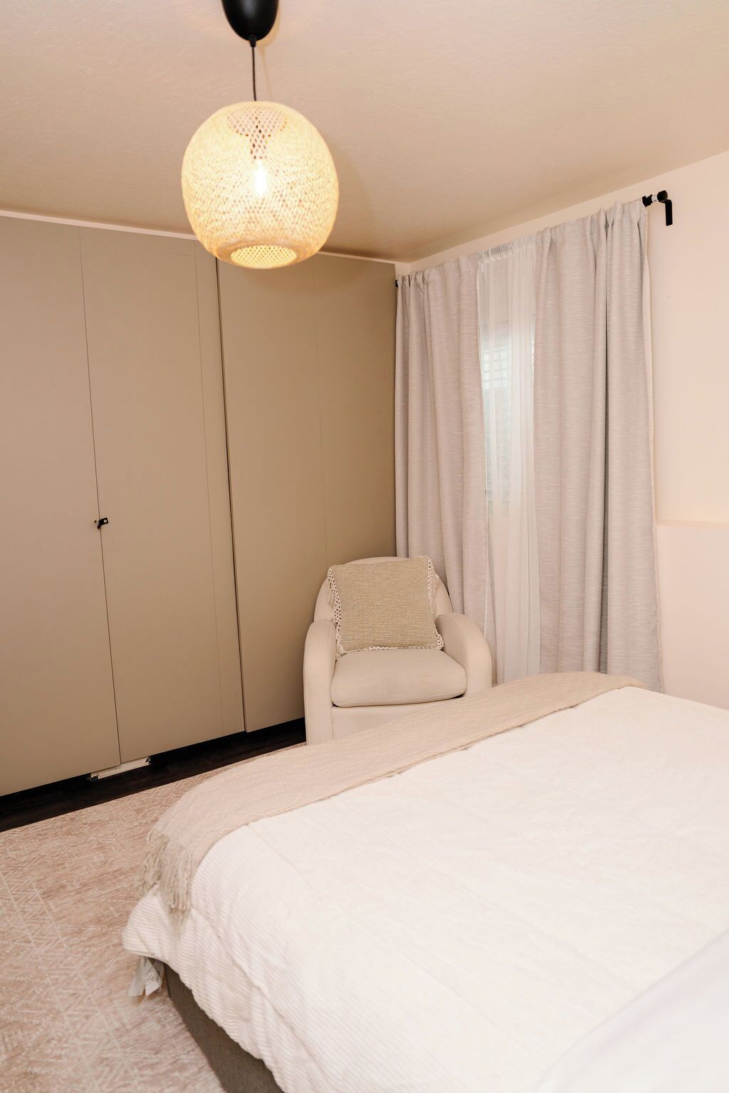 A bedroom with a bed, a chair, a wardrobe, and a hanging light fixture.