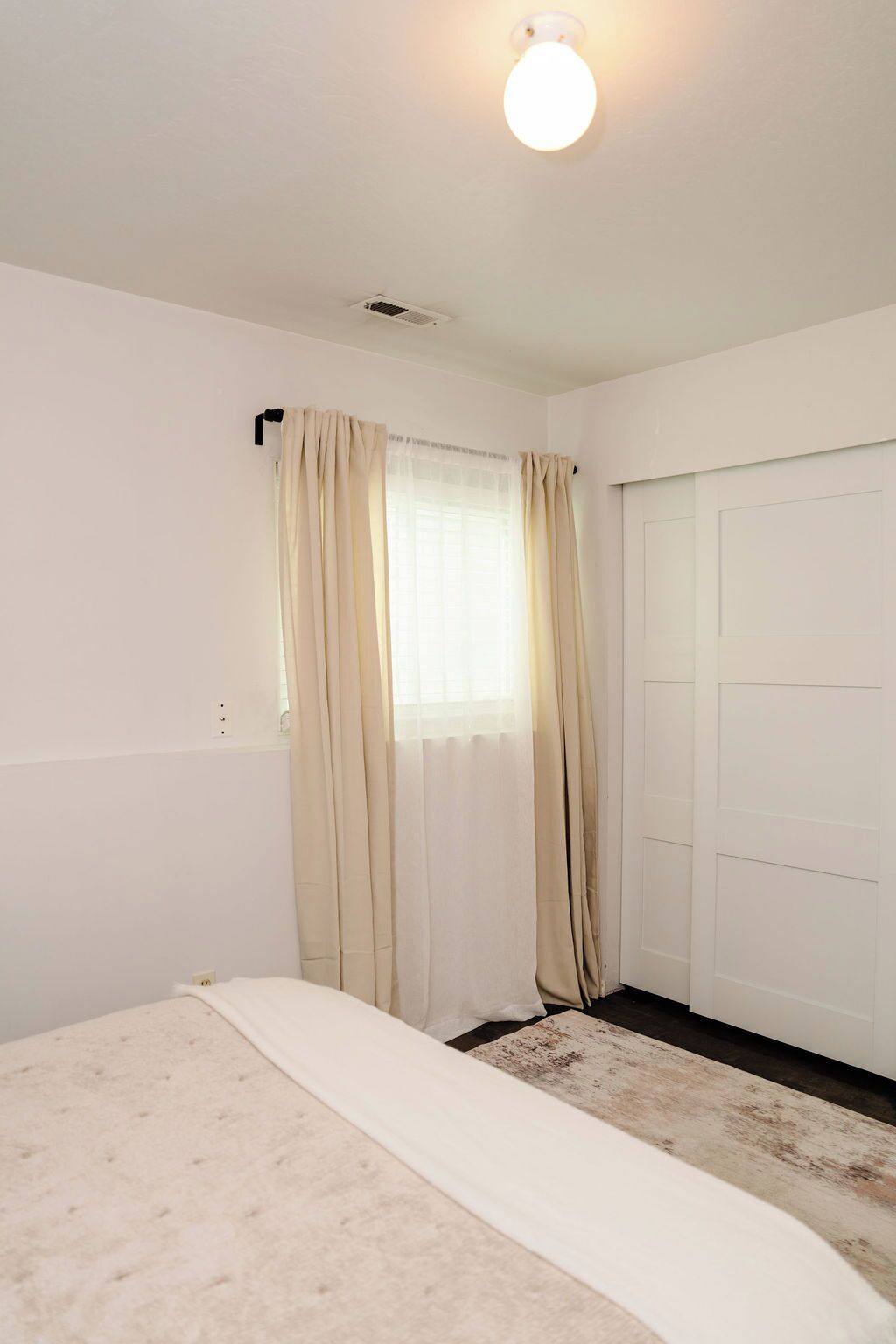 Un dormitorio con una cama, una ventana con cortinas, una puerta y una lámpara en el techo.