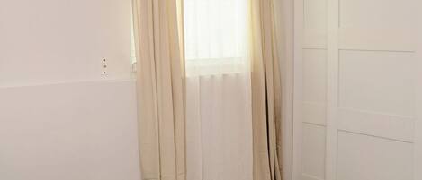 Un dormitorio con una cama, una ventana con cortinas, una puerta y una lámpara en el techo.