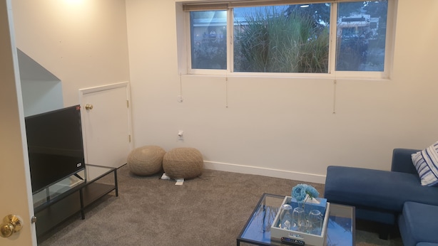 Een woonkamer met een televisie, twee ronde poufs, een glazen salontafel met een vaas, en een blauwe bank.