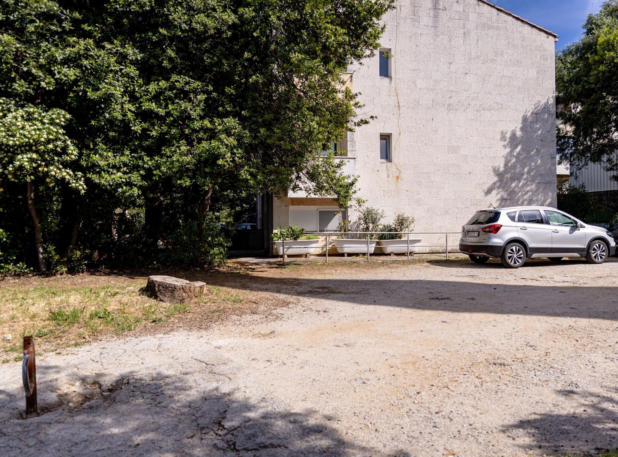 A building with a white exterior, a parked car, and a dirt ground.