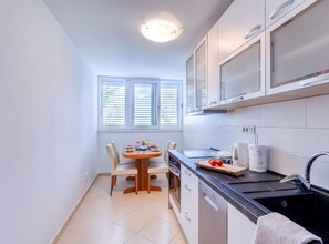 Eine kompakte Küche mit Esstisch, Backofen, Geschirrspüler und einem Fenster mit Jalousien.