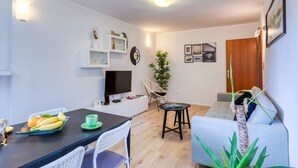 Ein modernes Wohnzimmer mit Fernseher, einem Esstisch mit Obst, einer Couch und einer Pflanze.