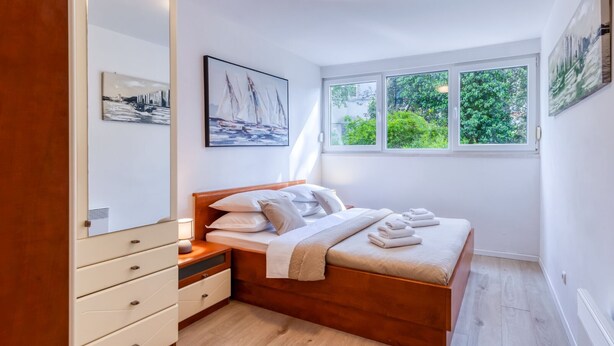 Ein Schlafzimmer mit einem hölzernen Bett, weißer Bettwäsche, einem Schminktisch mit Schubladen, einem großen Spiegel und einem Gemälde mit Segelbooten.