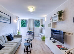 Ein modernes Wohnzimmer mit einer Couch, einem Esstisch, einem Fernseher und Pflanzen.