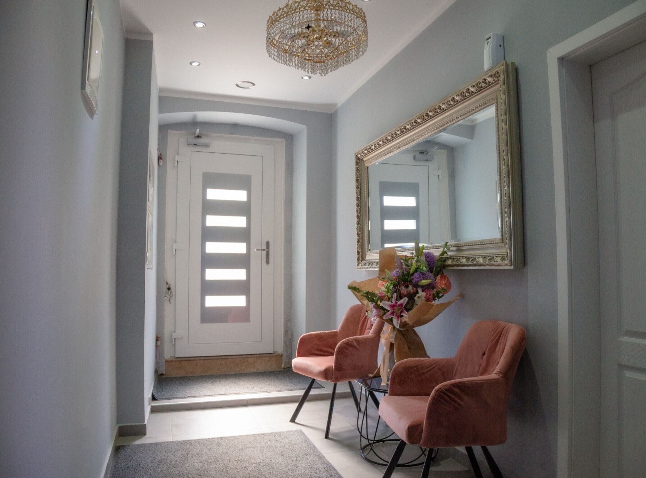 A hallway with a white door, a large mirror, and two pink chairs.