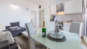 A modern living room with a glass dining table, grey sofa, and a kitchen in the background. - Comfrot One Bedroom Apartment with Sea View (Pula)