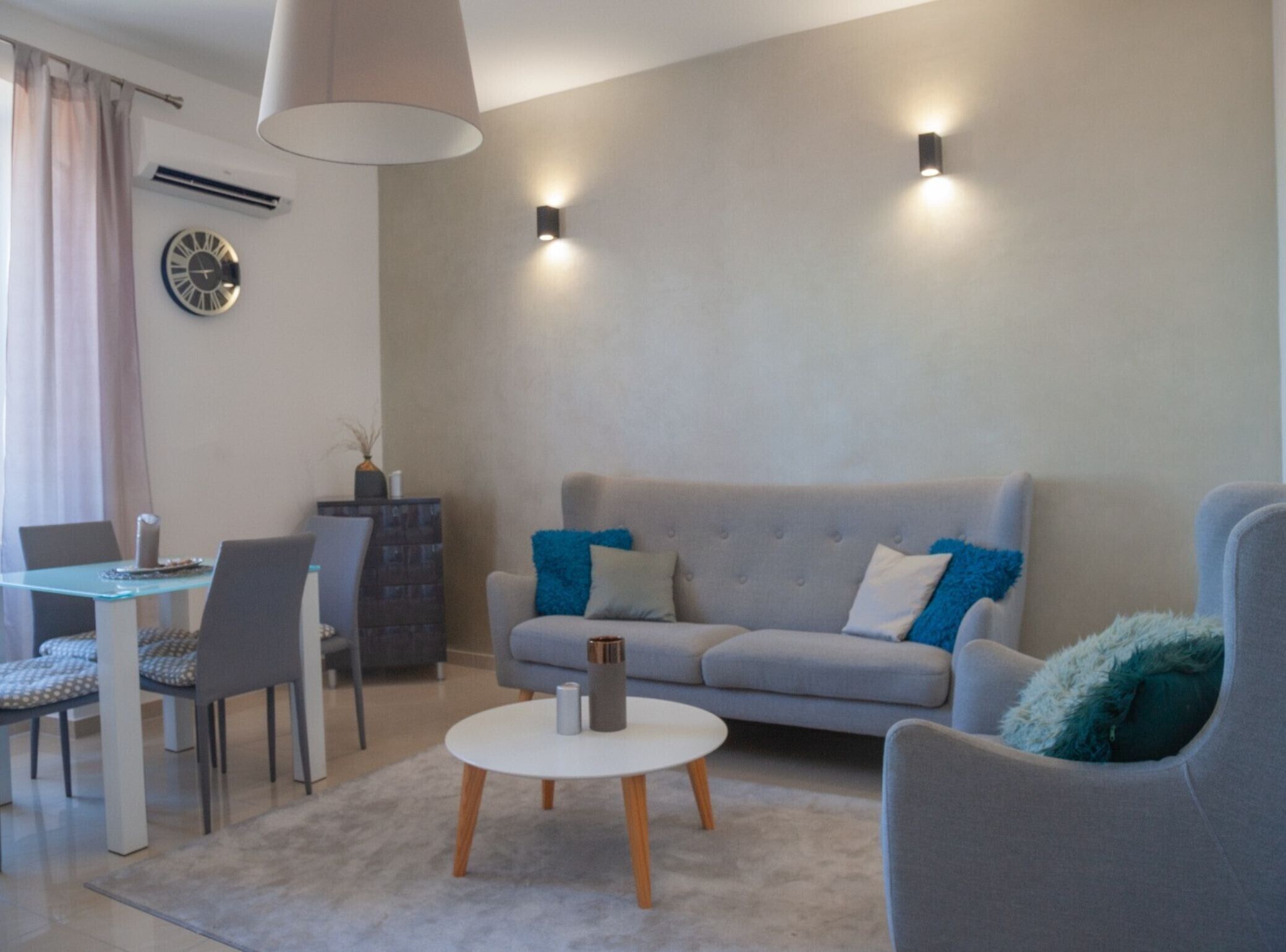 A modern living room with a grey sofa, a round coffee table, and a dining area with a table and chairs.