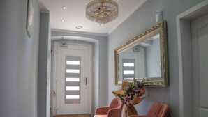 Un couloir avec une porte blanche, un grand miroir et deux chaises roses.