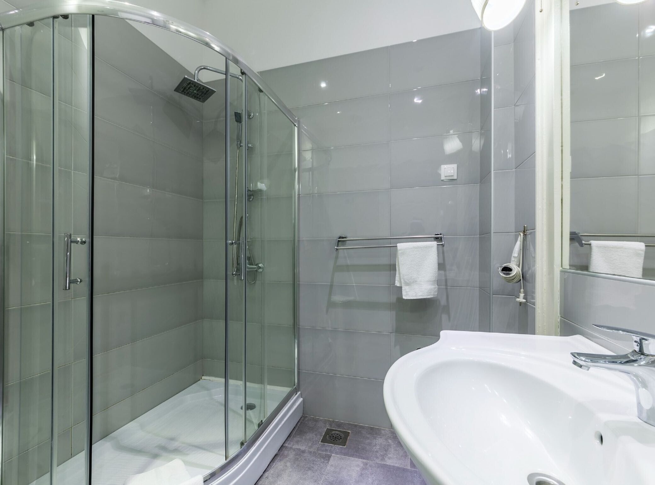 A modern bathroom with a glass-enclosed shower, a white sink, and a mirror.