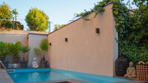 A swimming pool with a beige wall, potted plants, and Buddha statues. - Pula Garden Apartments with Shared Pool - Double Room (Pula)