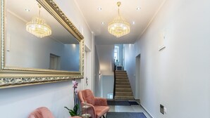 A hallway with a large mirror, two pink chairs, a small table with a plant, and a staircase in the background. - Pula Garden Apartments with Shared Pool - Double Room (Pula)