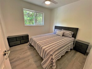 Una camera da letto con un letto, una finestra, una ventola a soffitto e comodini a muro.
