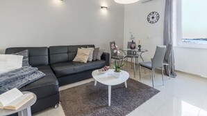 Een moderne woonkamer met een zwarte leren bank, een witte salontafel en een glazen eettafel.
