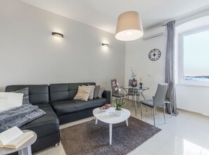 A modern living room with a black leather sofa, a white coffee table, and a glass dining table. - Classic One Bedroom Apartment with Sea View (Pula)
