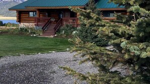 A log cabin with a green roof, a stone foundation, and a porch with a staircase. - Hebgen Paradise Lodge (West Yellowstone)