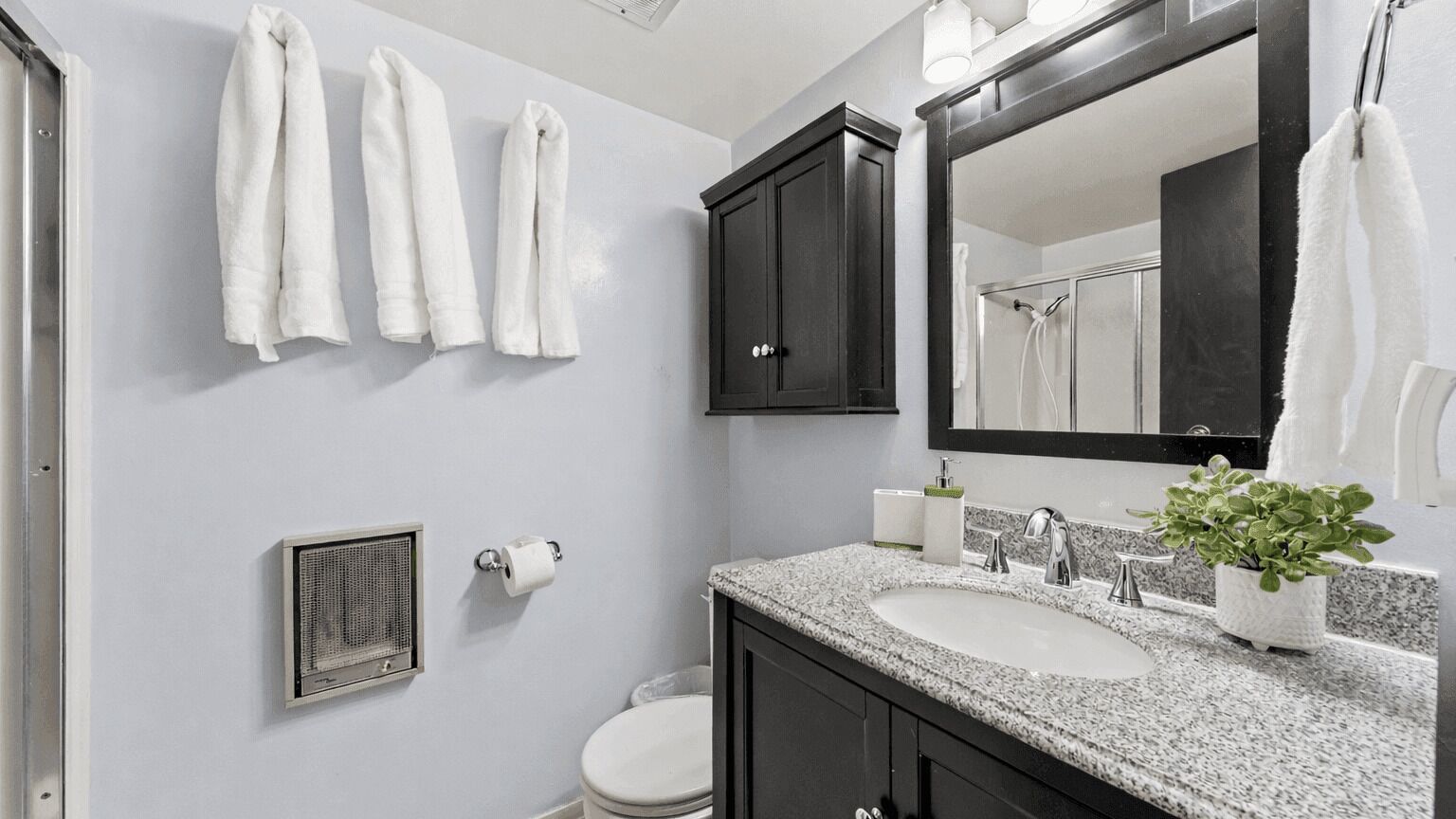 A bathroom with a sink, mirror, towel rack, toilet, and a ventilation unit.