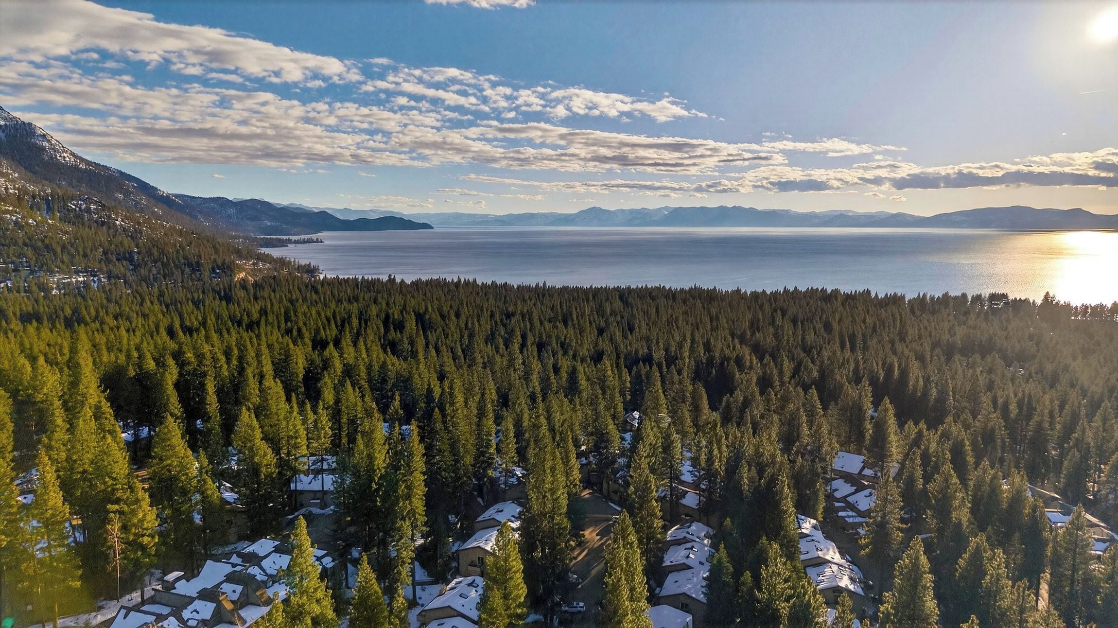 A forested area with snow-covered houses and a view of a large body of water.