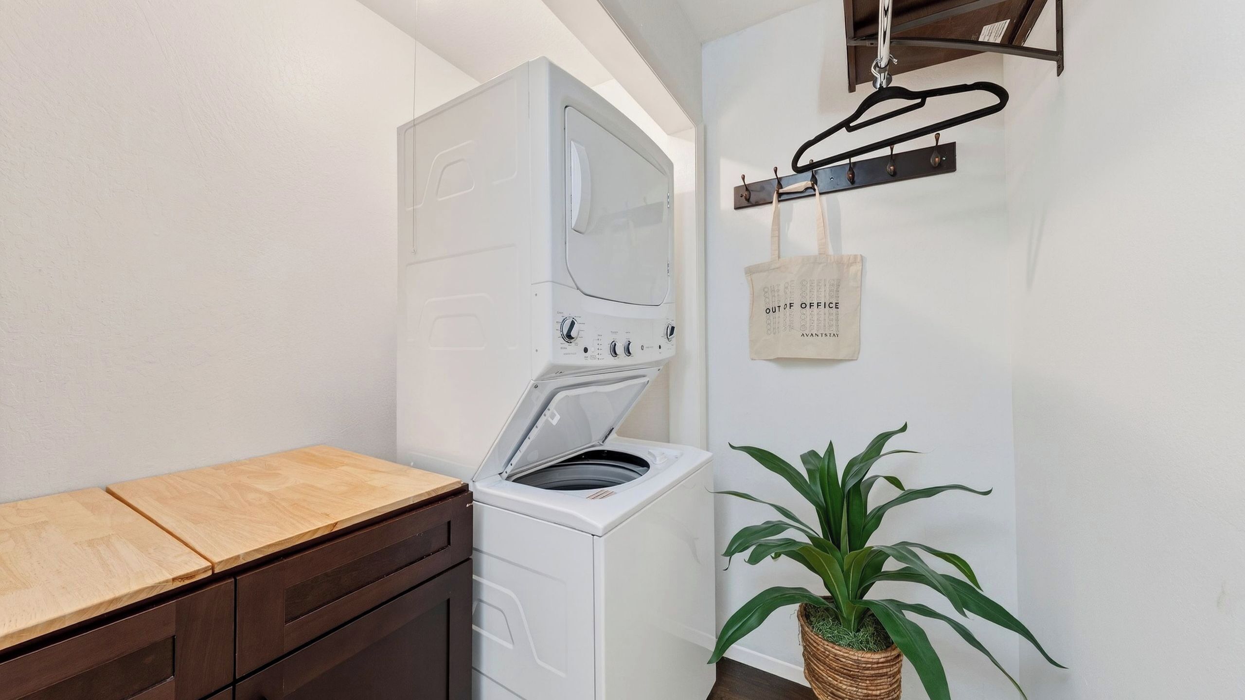 A laundry area with a washing machine, a drying rack, a wooden bench, and a potted plant.