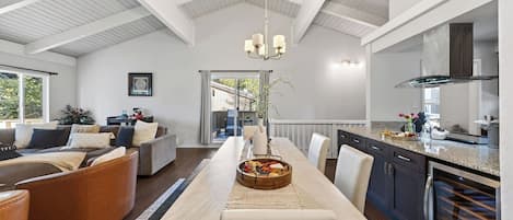 A spacious living area with a dining table, a kitchen with modern appliances, and a large window providing natural light.