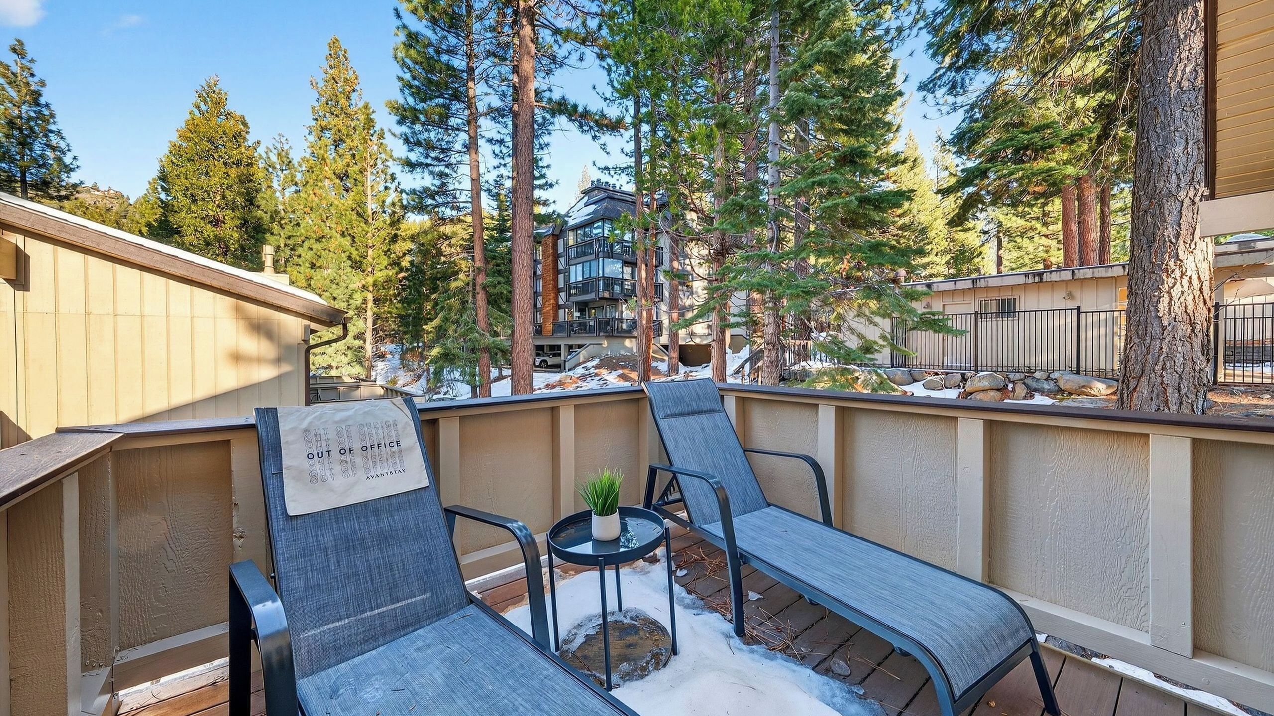 Une terrasse avec deux chaises et une petite table, entourée d’une clôture en bois et de grands arbres.