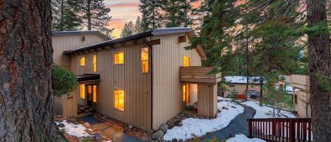 A multi-story wooden cabin with a covered porch and a stone pathway leading to the entrance.