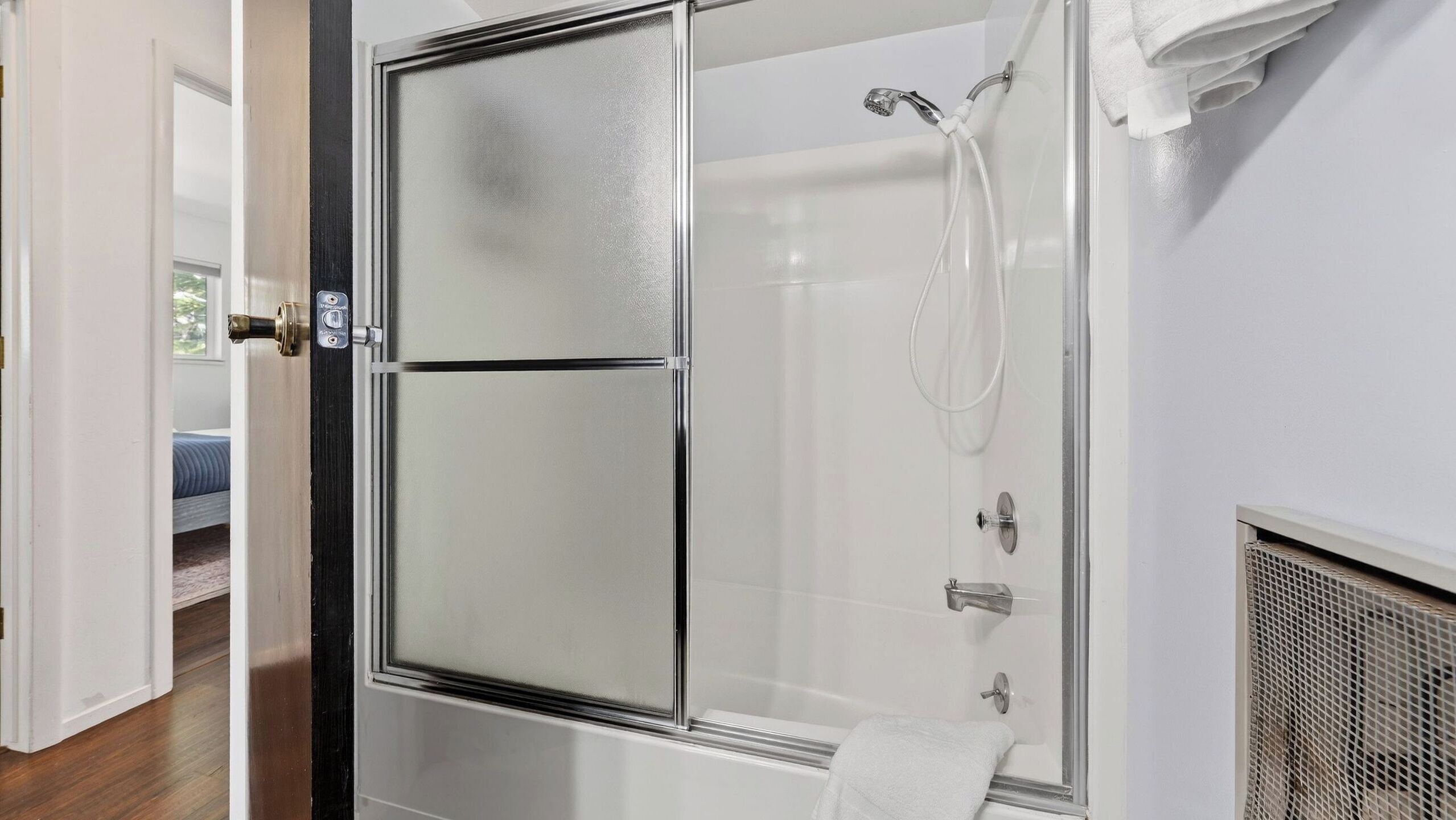 A modern bathroom with a glass shower enclosure, a visible towel, and a door leading to a bedroom.