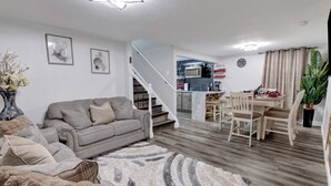 Ein modernes Wohnzimmer mit einem grauen Sofa, einem gemusterten Teppich und einem Essbereich mit Holzkohle und einem Tisch.