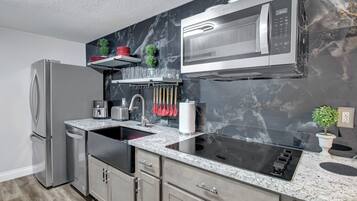 Una cucina moderna con frigorifero in acciaio inossidabile, forno a microonde integrato, lavello a due vasche e piano di lavoro in granito.