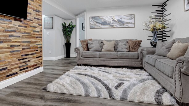Ein modernes Wohnzimmer mit grauem Sofa, einem flauschigen Teppich, einer Holzvertäfelung und einer Deckenleuchte.