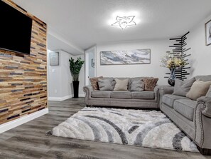 A modern living room with a grey sofa, a fluffy rug, a wooden accent wall, and a ceiling light fixture. - 3-bed/1 bath basement apartment in Aurora, CO w/AC~close to Hospitals (Aurora)