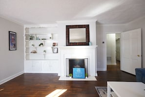 A living room with a white fireplace, white shelves, and a blue sign.