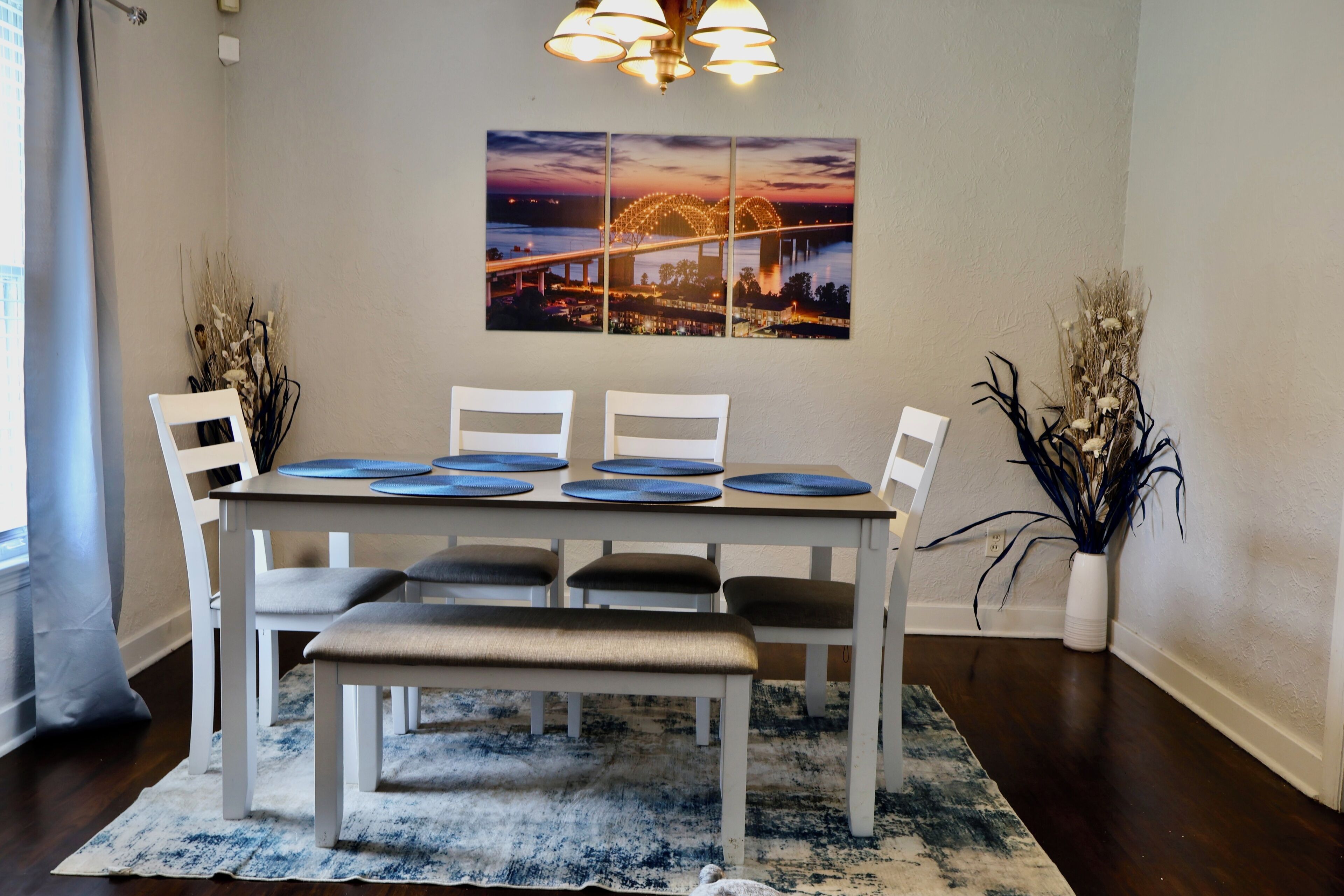 A dining area with a table, chairs, a bench, a rug, and a wall-mounted picture.