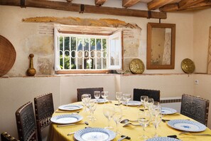 Una mesa de comedor dispuesta con platos, vasos y cubiertos, rodeada de sillas de madera con detalles metálicos.