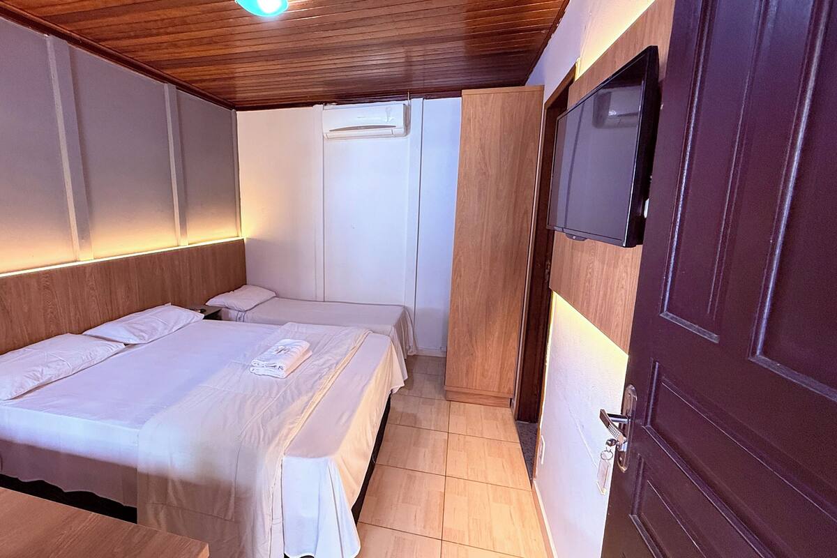 A hotel room with a wooden ceiling, two beds with white linens, a flat-screen TV mounted on the wall, and a wooden door.