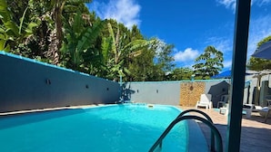 Una piscina con agua cristalina azul, rodeada de un muro de piedra y abundante vegetación.