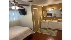 A bedroom with a bed, a ceiling fan, a television, a bathroom with a sink, mirror, and a toilet. - My family’s little nest, where our kids grew. (Perryton)