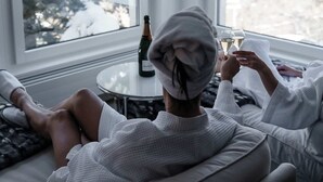 A room with two large windows, a bottle of wine, and a glass on a small table.