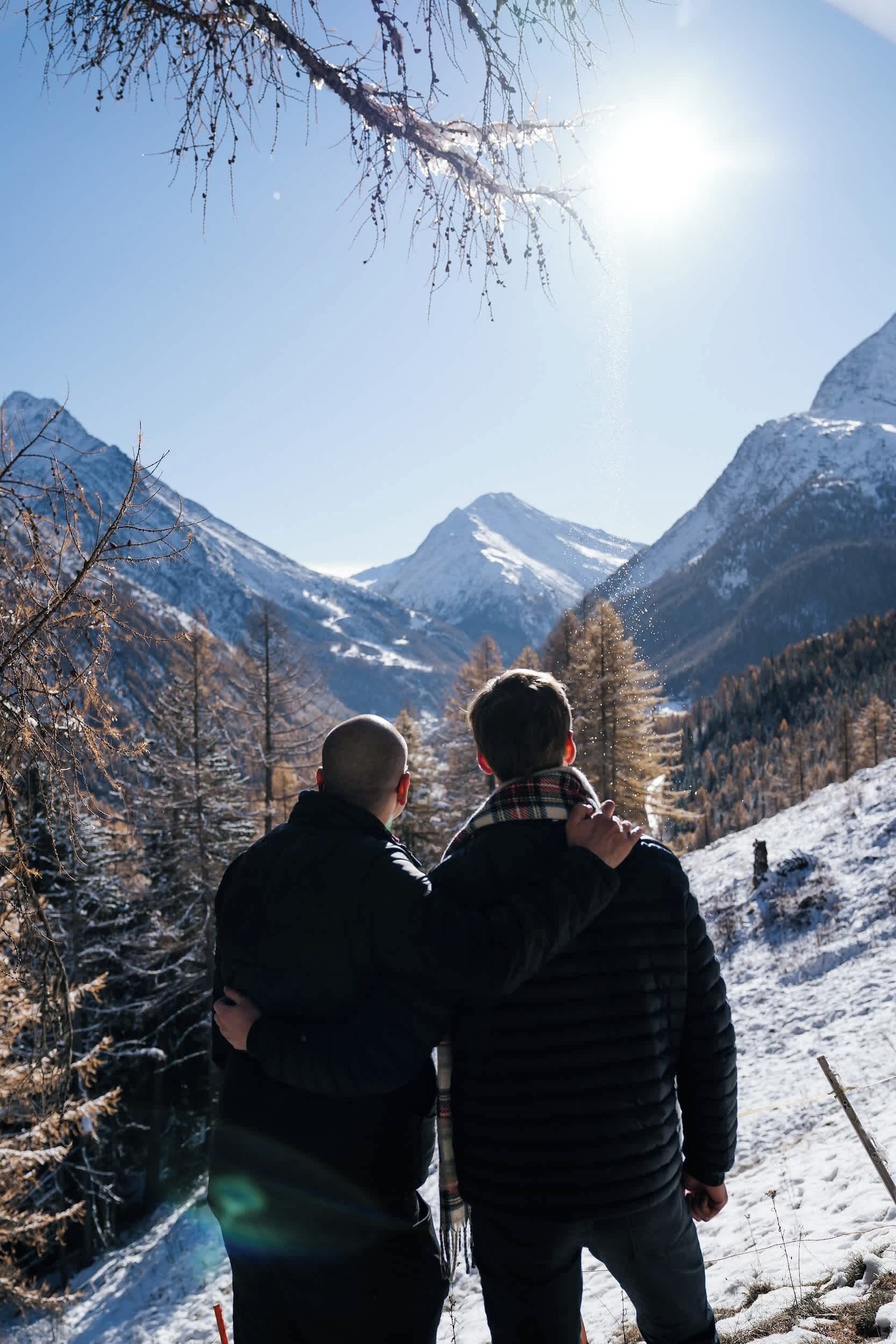 Two people standing on a snowy mountain with a clear sky and a mountain in the background.