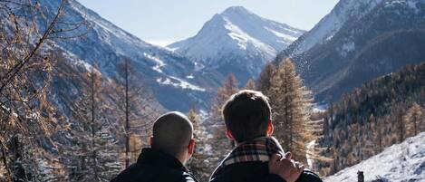 Two people standing on a snowy mountain with a clear sky and a mountain in the background.