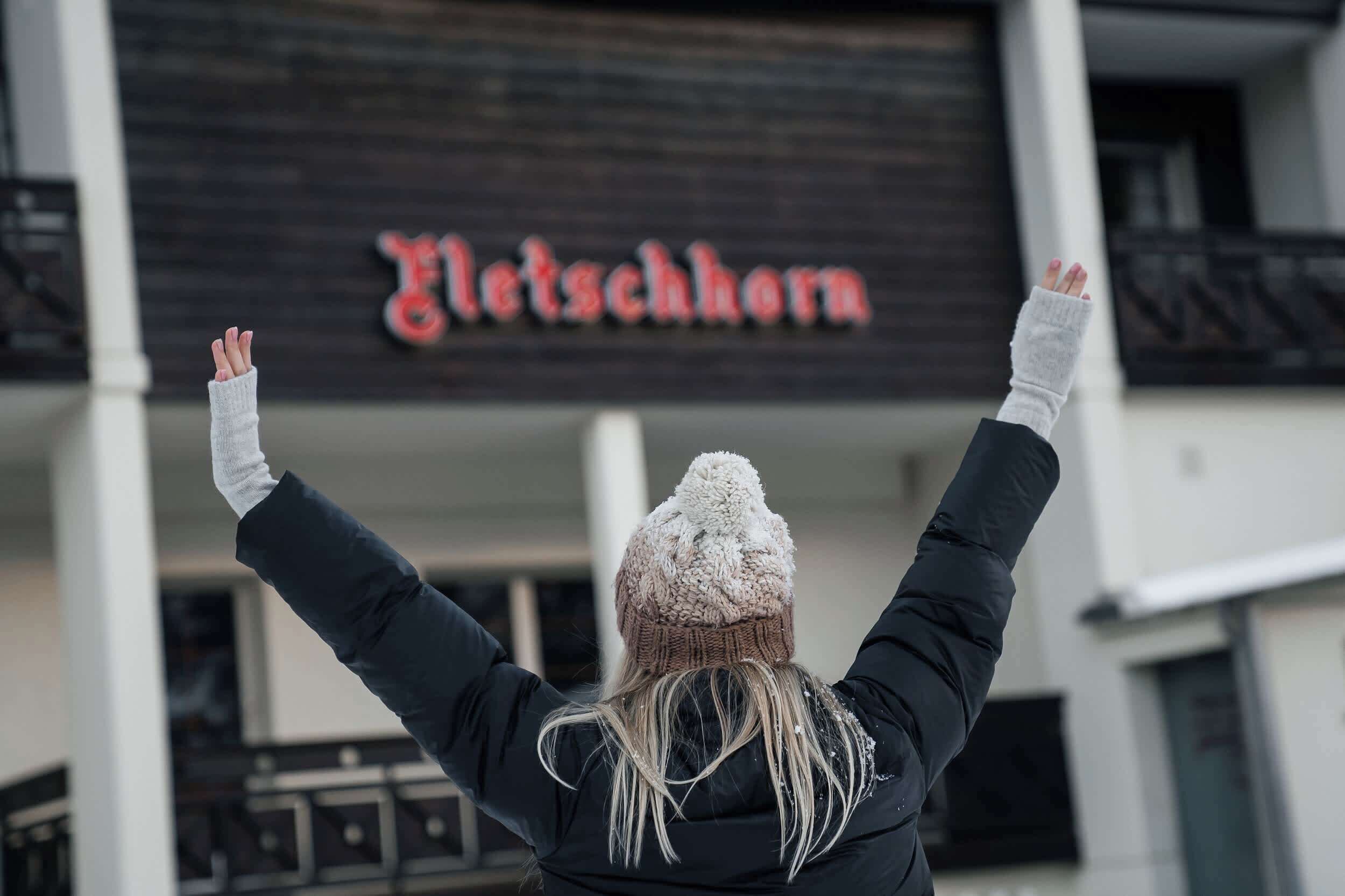 A person with arms raised in front of a building with a sign that reads "Gletscherhorn".