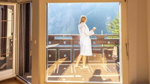 A room with a large sliding glass door leading to an outdoor balcony with a wooden deck and a view of mountains.