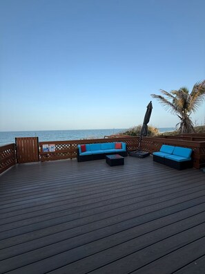 A wooden deck with blue outdoor seating and a view of the ocean.